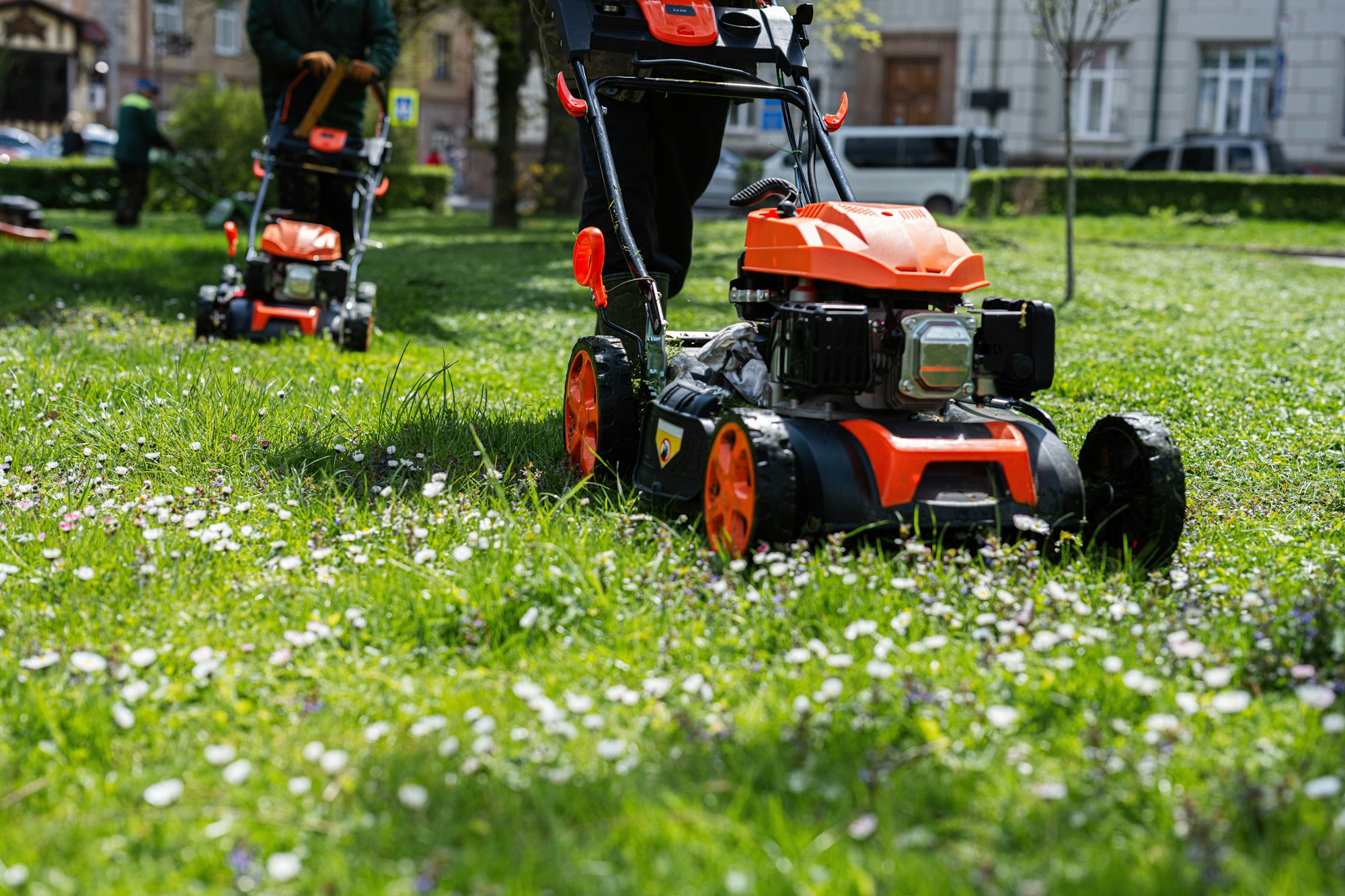 Communal services gardener worker man using lawn mower for grass cutting in city park.